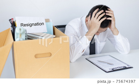 Businessman held his temple with his hand and had a brown document box beside it, Businessmen hand in resignation papers and packing office supplies in boxes with regret or disappointment. 75674397