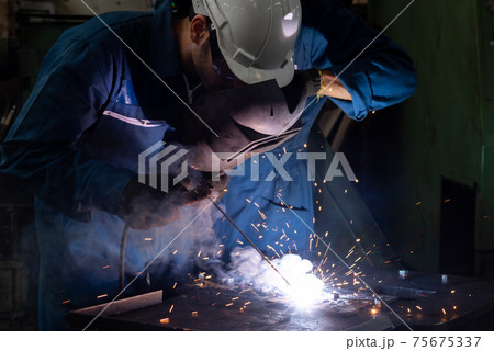 Skillful metal worker working with arc welding machine in factory 75675337