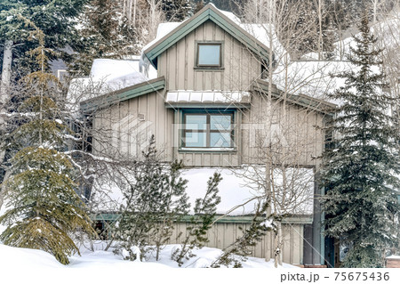 Exterior of home in the mountains with gray wall and snow covered roof in winter 75675436