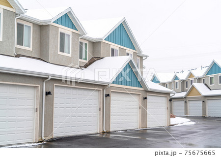 Apartment building exterior with white garages and pitched roofs against sky 75675665