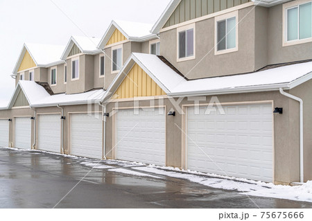 Wet road along white garage doors of apartment building against cloudy sky 75675666