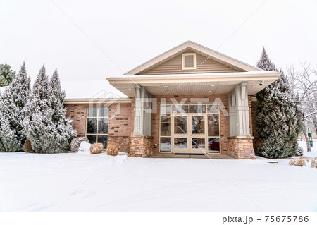 Building facade framed with lush snowy evergreens against cloudy sky in winter 75675786