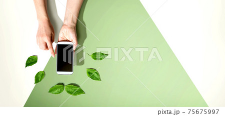 Person holding smartphone with green leaves 75675997