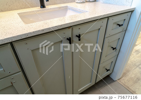White countertop with sink and black faucet over cabinets with black handles 75677116