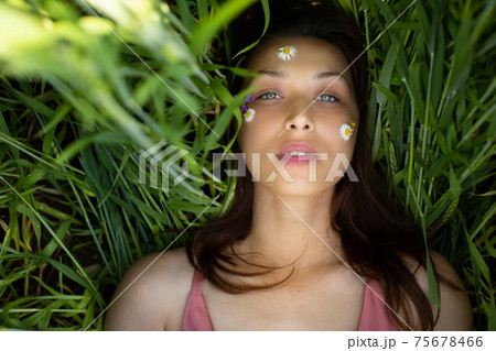 beautiful woman lies in green wheat with wild flowers and daisy glued on face 75678466