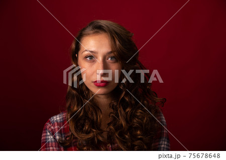 portrait of Beautiful curly long hairy model in plaid shirt posing on red studio 75678648