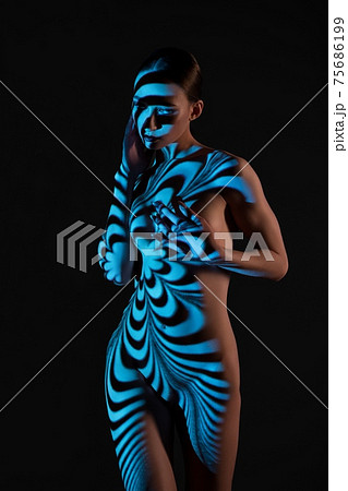 Nude woman standing in dark studio with striped illumination Nude woman standing in dark studio with striped illumination 75686199
