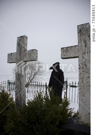 Medieval plague doctor stands on winter graveyard 75688813