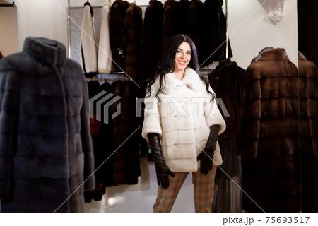 Happy joyful girl posing in white mink coat in a fur store 75693517