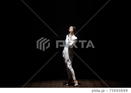 model in a white suit on stage in a beam of white light 75693699