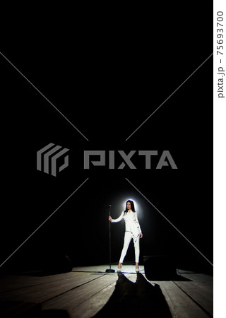 Singer woman on stage with black background in a beam of white light. 75693700
