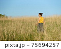 Beautiful woman in yellow shirt and long skirrt standing elegant in beige wheat field. Back view, bright blue sky 75694257