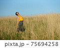 Beautiful woman in yellow shirt and long skirrt standing elegant in beige wheat field. Background of bright blue sky 75694258