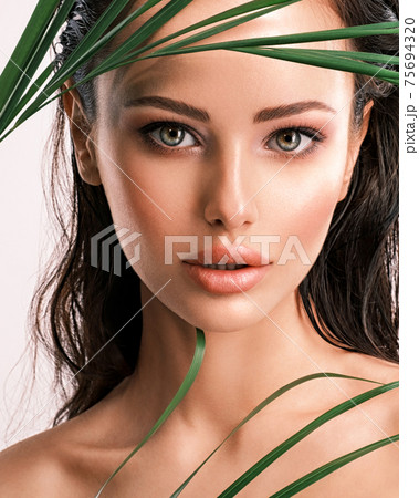 Young beautiful woman with green leaves near face and body. Skin care beauty treatments concept.  Closeup girl's face with green leave. White model with clean, health skin of face - posing at studio 75694320