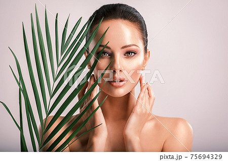 Young beautiful woman with green leaves near body. Skin care beauty treatments concept.  Closeup girl's face with green leaves. 75694329