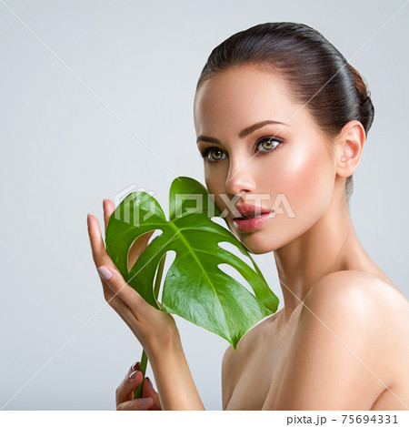 Beautiful woman with green leave near face and body. Closeup girl's face with green leave. Skin care beauty treatments concept. Beautiful woman with green leave near face and body. Closeup girl's face with green leave. Skin care beauty treatments concept. 75694331