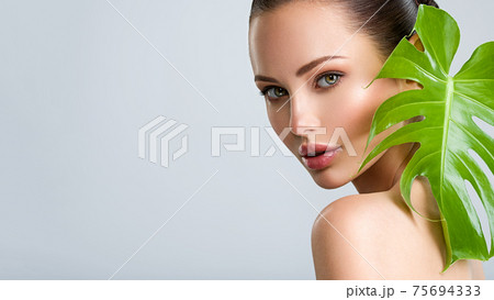 Beautiful woman with green leave near face and body.  Closeup girl's face with green leave. Skin care beauty treatments concept. 75694333