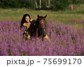 Beautiful woman with long hair in yellow dress riding bareback a brown horse in among purple flowers in green field 75699170