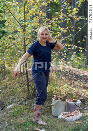 A girl with a knife in her hand stands next to buckets of mushrooms 75700613
