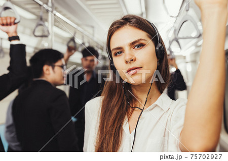 Beautiful young woman passenger standing with headphones and while shirt in the modern subway train Beautiful young woman passenger standing with headphones and while shirt in the modern subway train 75702927