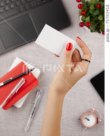 Woman with red manicure holding blank business card on gray table 75703418