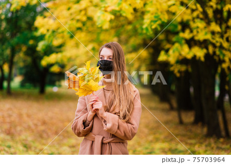 Portrait of a beautiful adult young woman on the background of autumn in park in medical face mask 75703964