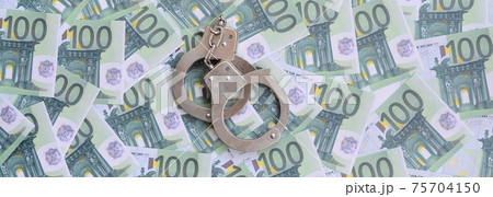 Police handcuffs lies on a set of green monetary denominations of 100 euros. A lot of money forms an infinite heap Police handcuffs lies on a set of green monetary denominations of 100 euros. A lot of money forms an infinite heap 75704150