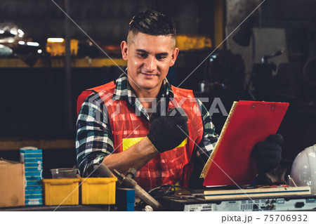 Factory worker talking on portable radio while inspecting machinery parts 75706932