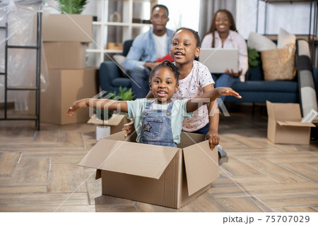 Two little african girls kids playing with boxes while parents relaxing on sofa at modern appartment Two little african girls kids playing with boxes while parents relaxing on sofa at modern appartment 75707029
