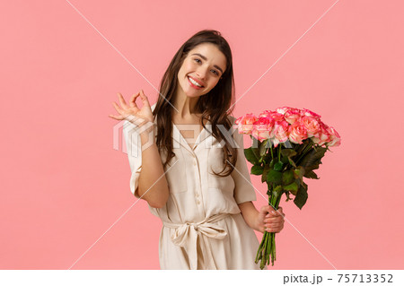Lovely, dreamy and coquettish brunette female in dress, tilt head and smiling delighted, showing okay, good holding roses, got gift on valentines day, beautiful bouquet flowers, pink background Lovely, dreamy and coquettish brunette female in dress, tilt head and smiling delighted, showing okay, good holding roses, got gift on valentines day, beautiful bouquet flowers, pink background 75713352