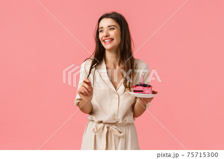 Celebration, happiness and holidays concept. Beautiful young woman having fun, holding plate with cake, smiling and laughing carefree, eating b-day dessert blowing-out candle, having fun 75715300