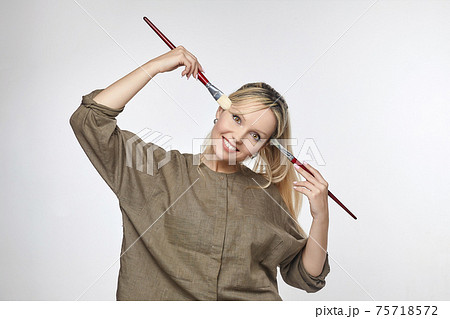 young artist poses in front of the camera, pressing her brushes to her temples 75718572
