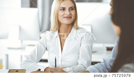 Group of business people discussing questions at meeting. Headshot of blonde businesswoman while smiling to her colleague at office negotiation. Teamwork and cooperation in corporate occupation Group of business people discussing questions at meeting. Headshot of blonde businesswoman while smiling to her colleague at office negotiation. Teamwork and cooperation in corporate occupation 75725079