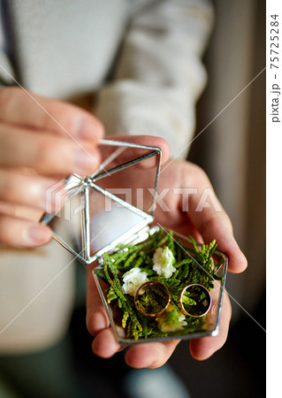 Groom men holding wedding rings lie on a beautiful, decorative hand made rustic box with plants Groom men holding wedding rings lie on a beautiful, decorative hand made rustic box with plants 75725284