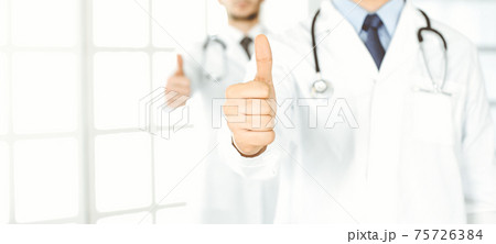 Two male doctors standing as a team with thumbs up in hospital office and ready to help patients. Medical help, best disease treatment and medicine concept 75726384
