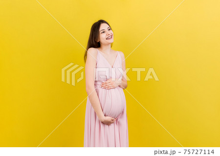 Happy pregnant woman touching her abdomen at Colored background. Future mother is wearing white underwear. Expecting of a baby. Copy space Happy pregnant woman touching her abdomen at Colored background. Future mother is wearing white underwear. Expecting of a baby. Copy space 75727114