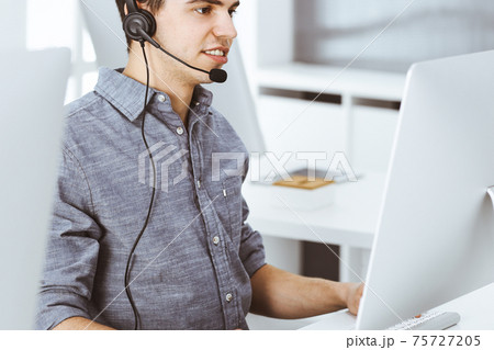 Casual dressed young man using headset and computer while talking with customers online. Call center, business concept 75727205