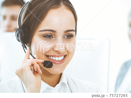 Call center. Group of diverse operators at work. Beautiful woman in headset communicating with customers of telemarketing service. Business concept 75727265