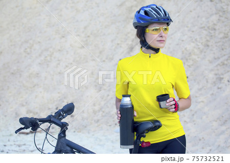Beautiful girl cyclist in yellow with tea and thermos in hand 75732521