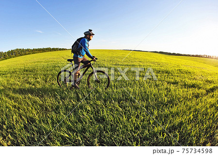 cyclist rides a bicycle on the green field towards the sun 75734598