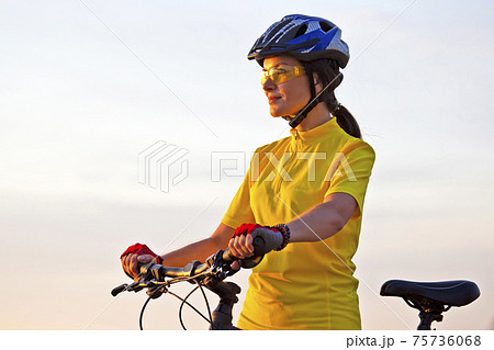 Beautiful girl in a yellow cyclist on a bike reaches in sunlight 75736068