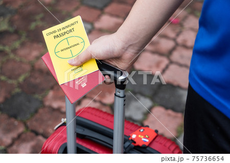 Traveller pulling luggage with conceptual Covid-19 Immunity Passport on hand Traveller pulling luggage with conceptual Covid-19 Immunity Passport on hand 75736654