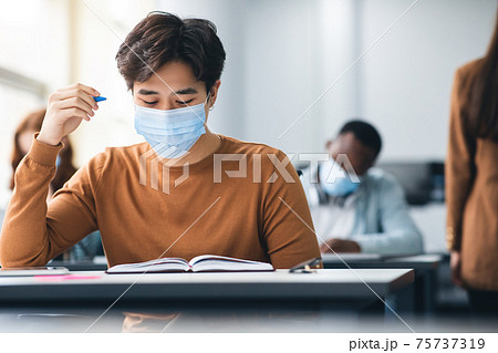 Male asian student in mask sitting at desk in class Male asian student in mask sitting at desk in class 75737319