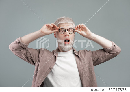 Surprised albino blond man touching glasses with open mouth, guy posing over grey studio background Surprised albino blond man touching glasses with open mouth, guy posing over grey studio background 75737373