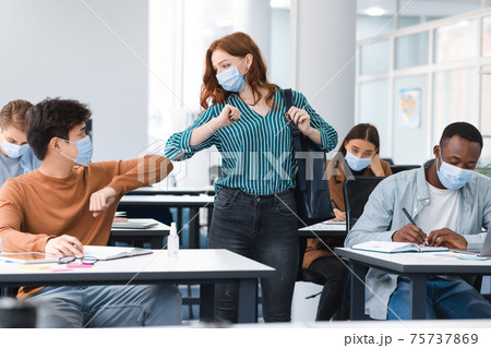 Diverse people wearing disposable face masks greeting and bumping elbows 75737869