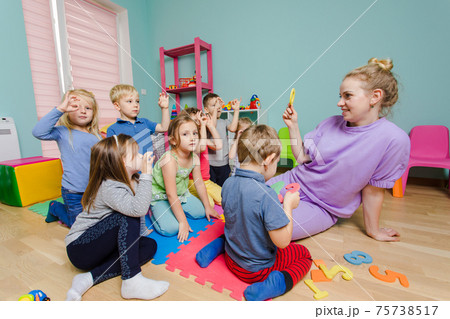 Preschool teacher teaching group of children, sitting on a floor 75738517