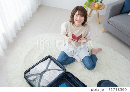 リビングでパスポートを眺めながら旅行の準備をする若い女性 75738560