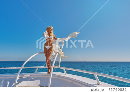 Young woman standing on the deck of a boat in open sea at sunny summer day 75740022