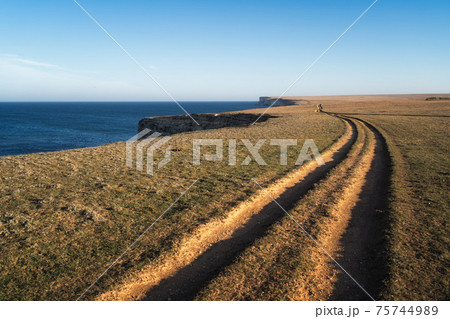 A gravel road leading toward horizon. Spectacular view on the sea and blue sky in the evening. Panoramic image A gravel road leading toward horizon. Spectacular view on the sea and blue sky in the evening. Panoramic image 75744989