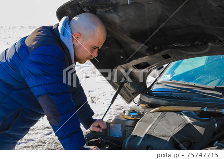 Young man looking under the hood of broken car in cold winter day Young man looking under the hood of broken car in cold winter day 75747715